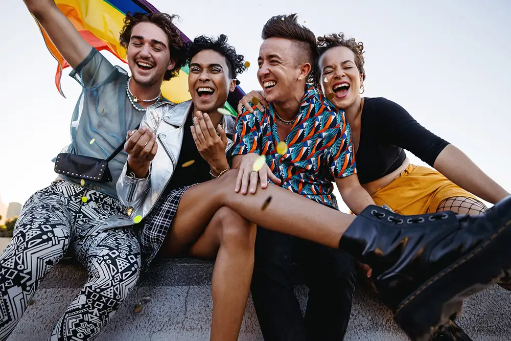 A group of friends laughing together holding a rainbow flag above them
