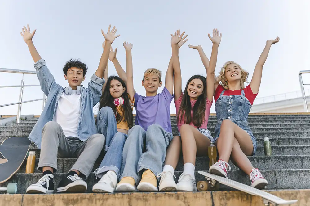 A group of young children sitting outside on stairs with their hands in the air in unison
